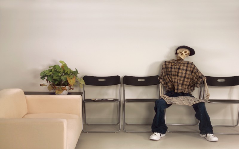Skeleton Man Sitting Waiting Room with Newspaper