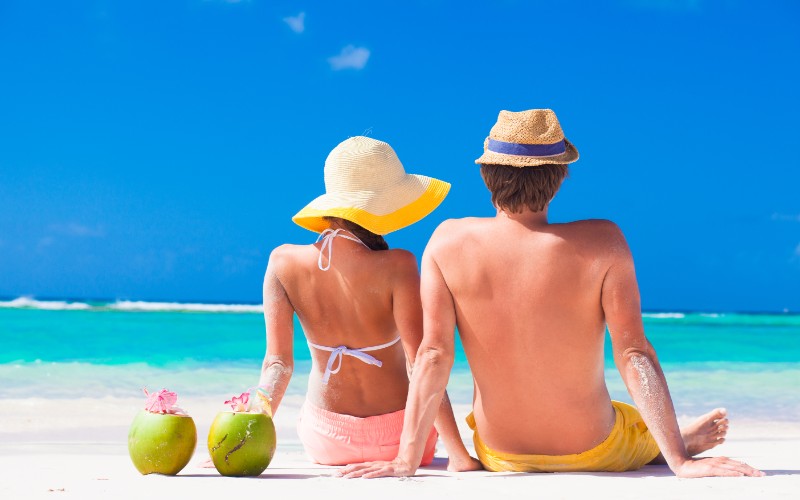 young couple sitting at tropical beach with coconut cocktail