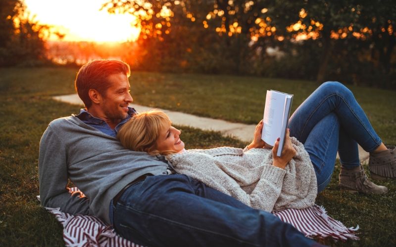 couple lying in grass reading a book together on blanket