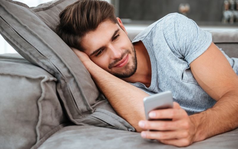 guy reading text/email on cell phone smiling laying on couch