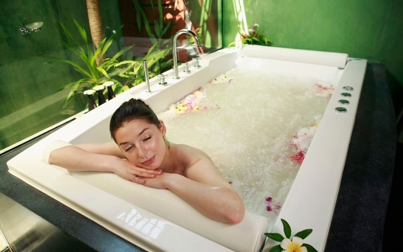 lady relaxing in hot bathtub with rose petals