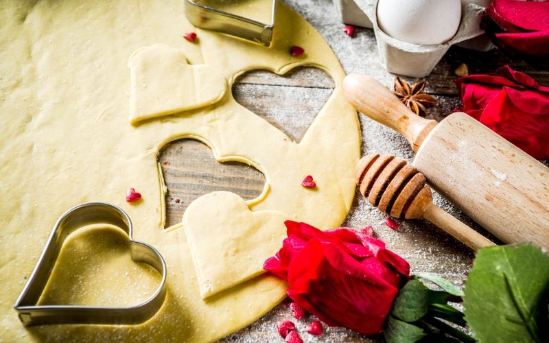 cookie dough with heart cut outs displayed with roses and pin roller