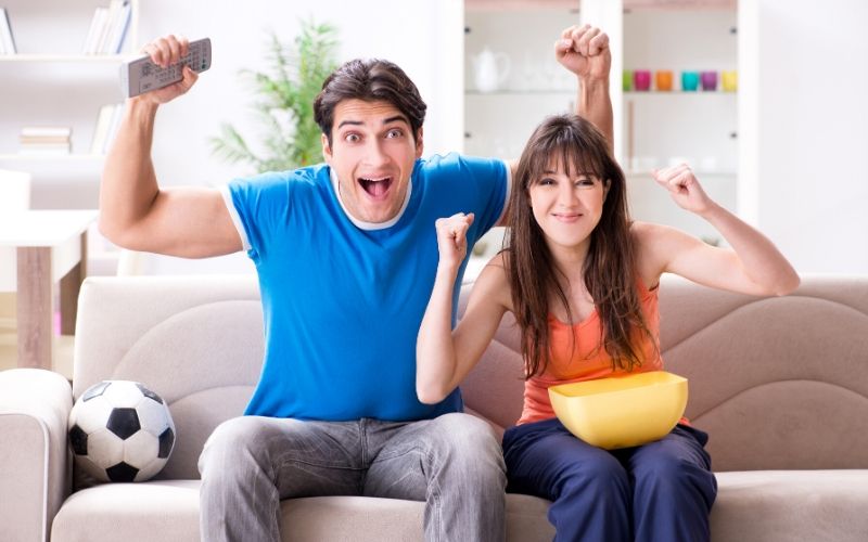 couple sitting on couch with soccer ball cheering for winning sports team