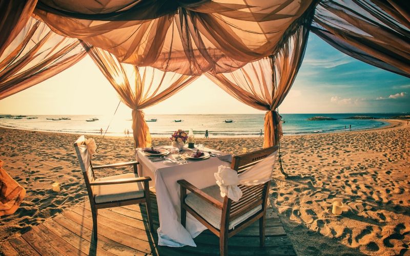 beach dinner table and chairs on beach decorated with shaded curtains on beach front