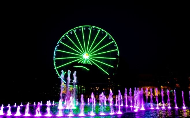 tall ferris wheel behind water show at night