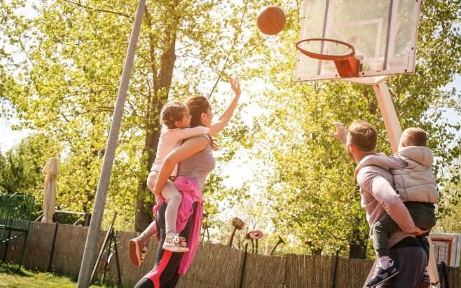 husband and wife playing outdoor basketball with children on their backs