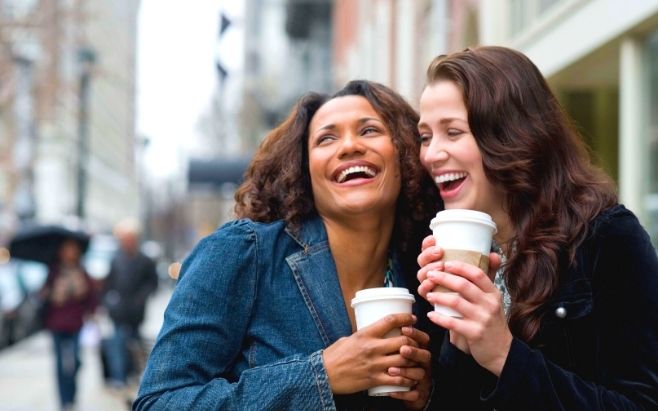 two women laughing while hanging out holding coffee cups