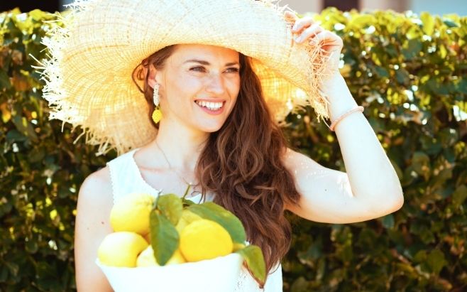woman smiling wearing a hat and carrying basket of lemons