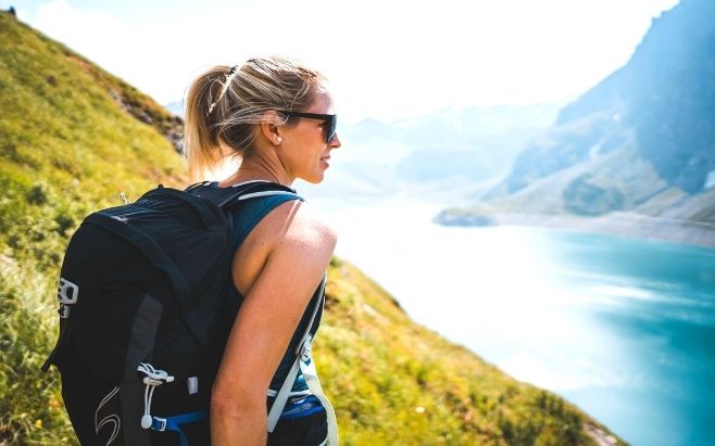 woman wearing backpack standing on top of cliff watching waterfront