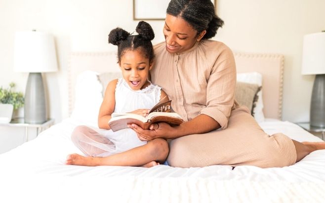 woman sitting up in bed next to daughter reading a book