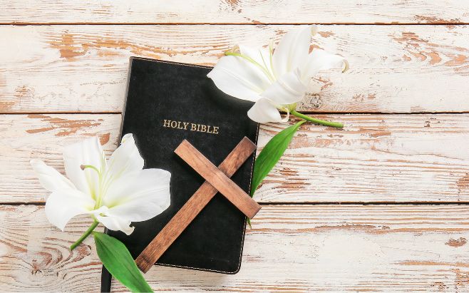 white flowers and cross on top of black Holy Bible
