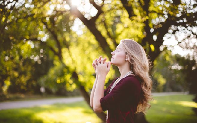 woman praying with eyes closed standing outside in nature