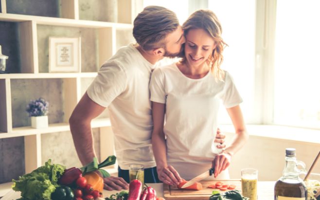 man kissing woman in kitchen as she cooks