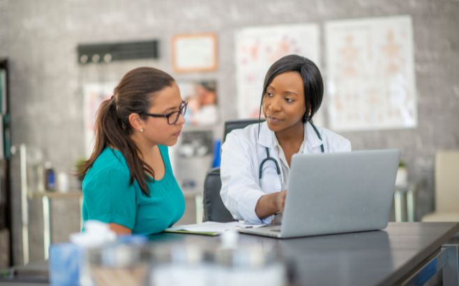 woman sitting with doctor as she points to laptop