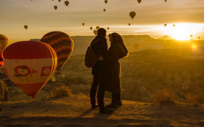 couple standing on top of hill surrounded by hot air balloons