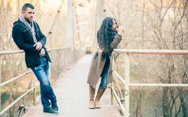 couple standing apart on bridge looking away from each other