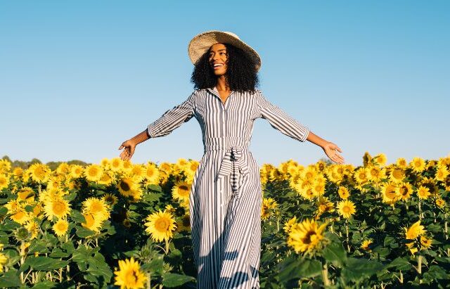 black woman standing with arms open in sunflower field