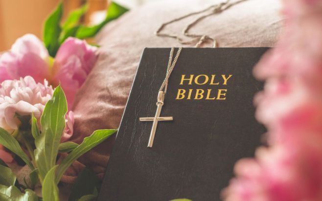 cross pendent hanging on Holy Bible surrounded by pink flowers