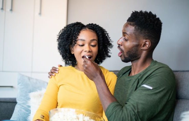 man feeding popcorn to woman sitting on couch