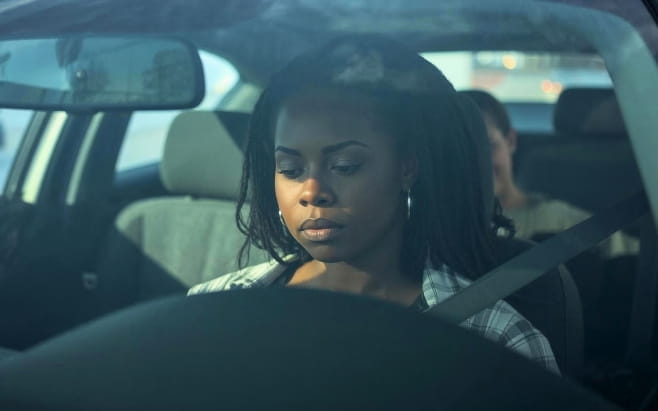woman sitting in front seat of a car thinking as child sits in back seat