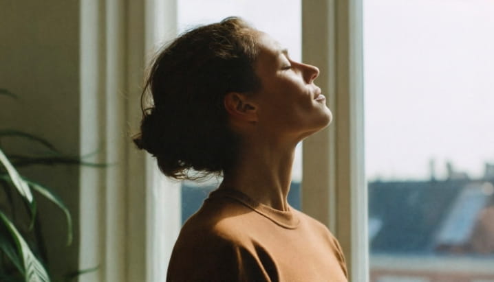 woman-standing-near-window-with-eyes-closed-with-sunlight-on-face