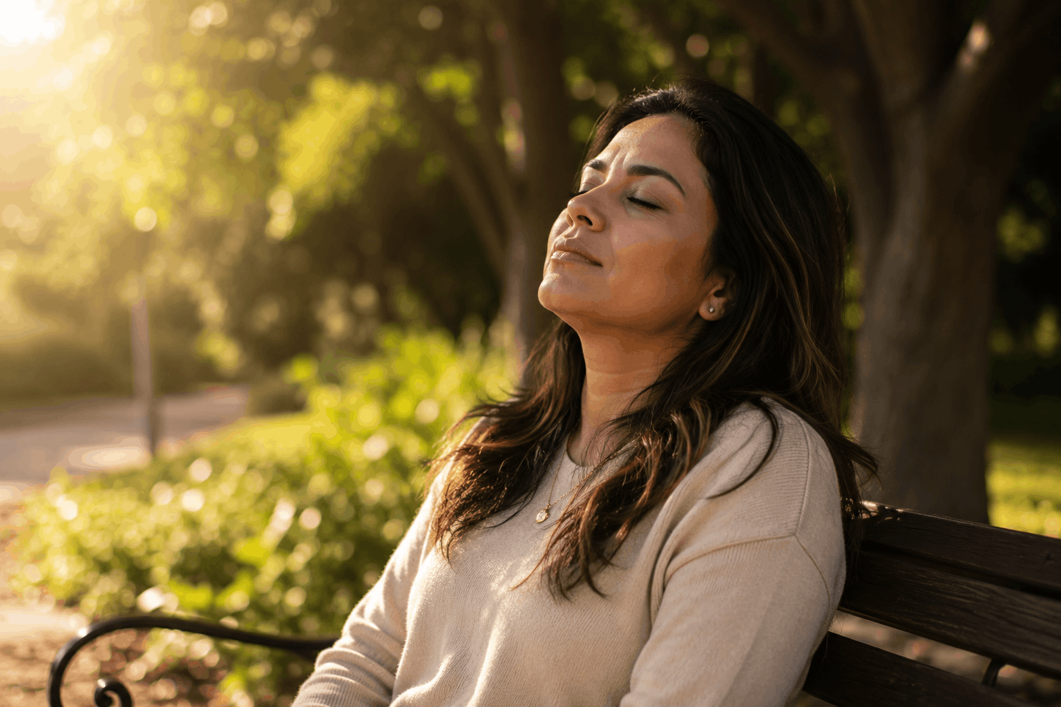 woman sitting on park bench with eyes closed feeling at peace